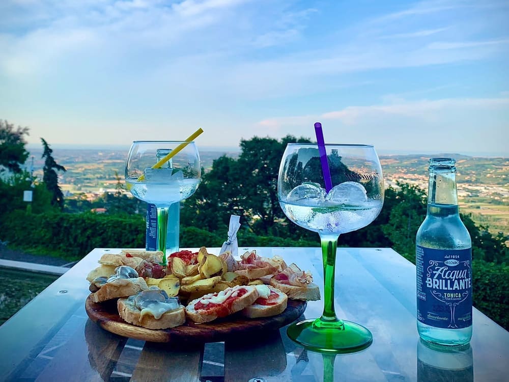 Due gin tonic e un piatto di crostini su un tavolino affacciato sulla Valmarecchia, con la valle e il cielo sullo sfondo
